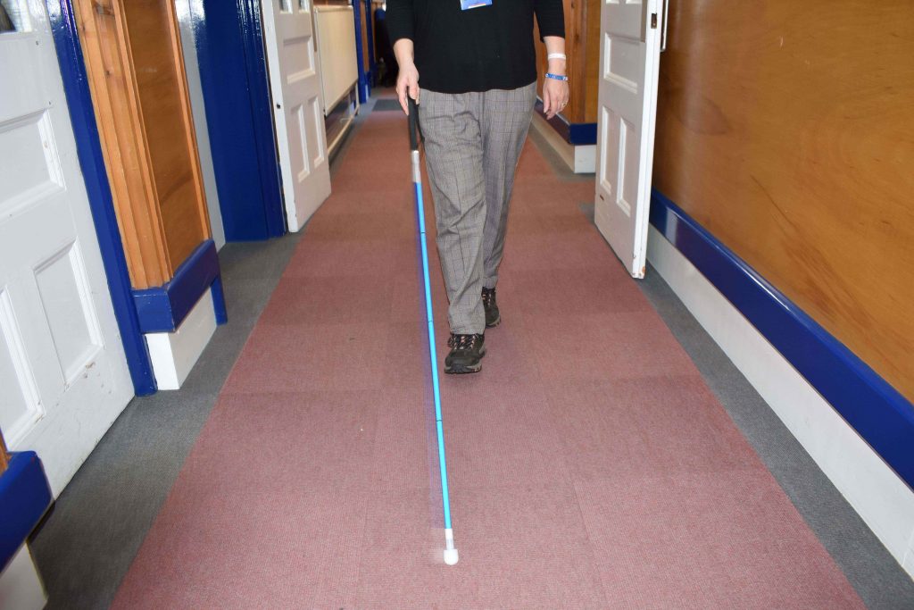 Image of a white cane being used in a hallway by a cane user