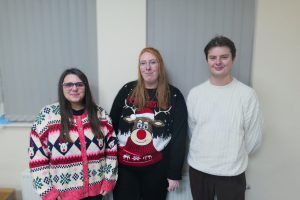 Image of two women and a man smiling wearing Christmas jumpers
