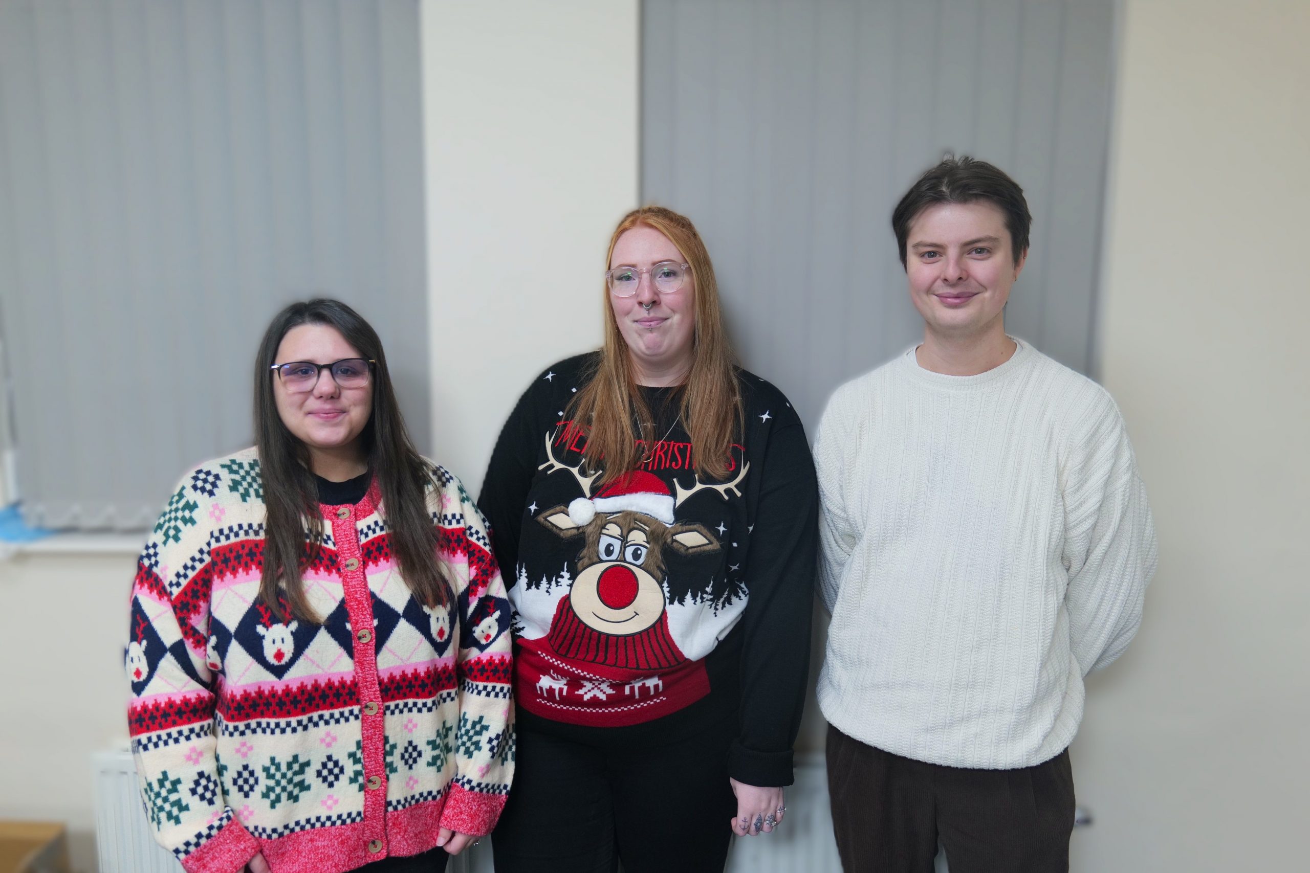 Image of two women and a man smiling wearing Christmas jumpers