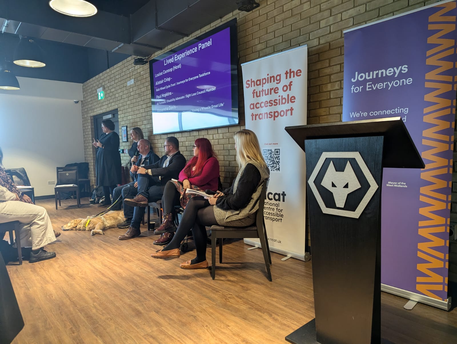 Image of Paul talking into a microphone alongside 4 panellists