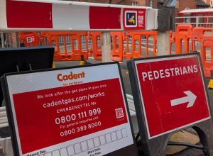 Image of two signs, one with information on works by Cadent and a red sign with pedestrians and an arrow pointing where to walk